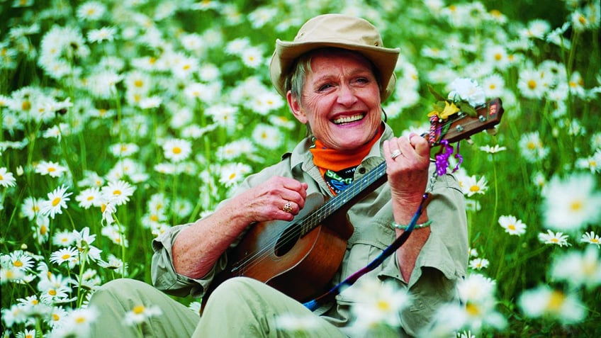 Sonja Christopher playing guitar in a field of flowers