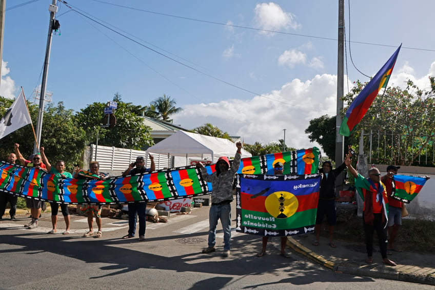 Protesters holding Kanak flags demonstrate as French President Emmanuel Macron's motorcade drives past in Noumea, France's Pacific territory of New Caledonia on May 23, 2024. Macron flew to France's Pacific territory of New Caledonia on a politically risky visit aiming to defuse a crisis after nine days of riots that have killed six people and injured hundreds. Macron's sudden decision to fly to the southwest Pacific archipelago, some 17,000 kilometres (10,500 miles) from mainland France, is a sign of the gravity with which the government views the pro-separatist violence. (Photo by Ludovic MARIN / POOL / AFP) (Photo by LUDOVIC MARIN/POOL/AFP via Getty Images)