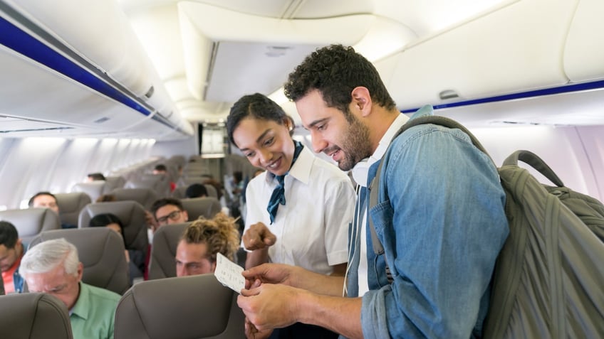 Flight attendant helping man find his seat in an airplane