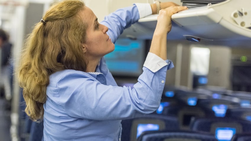 A woman reached in the overhead compartment on an airplane