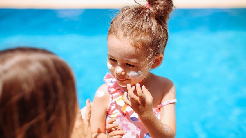 little girl putting on sunscreen with mom