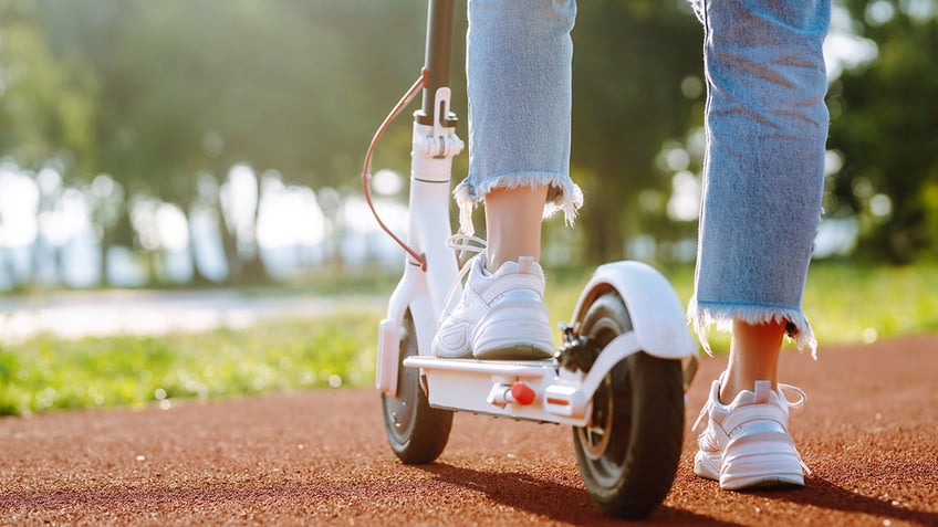 Woman riding electric kick scooter outdoors at sunset, closeup.