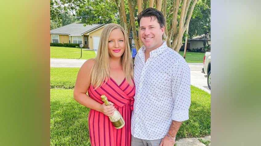 Andrea and Shawn Yarbrough pose outside with a bottle of wine.