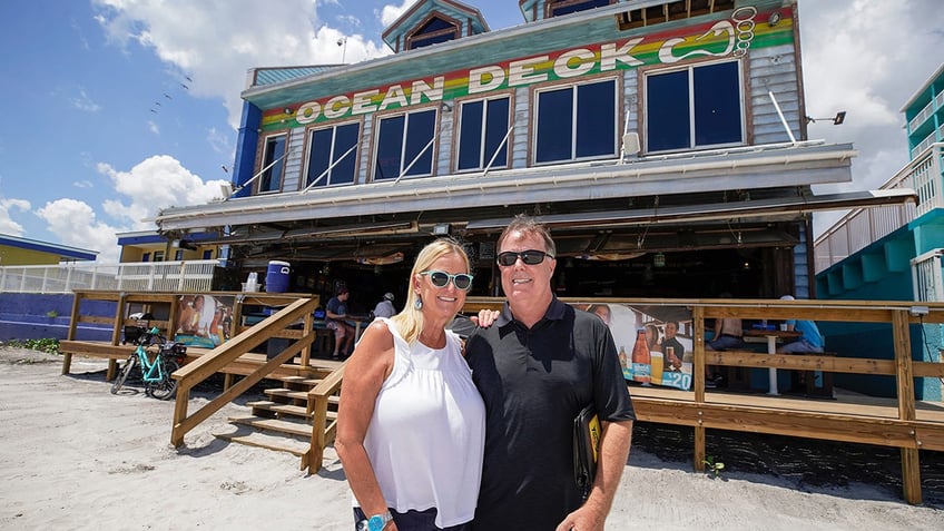 A woman and man wearing sunglasses pose outside the Ocean Deck Restaurant & Beach Club in Daytona Beach, Florida.