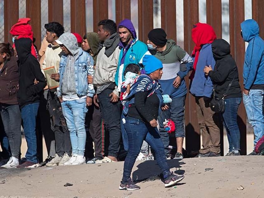 A migrant woman carries a child on her back while looking at the line of fellow migrants a