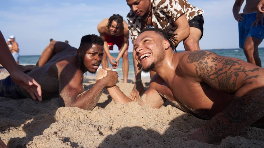 Spring breakers arm wrestle in the sand.