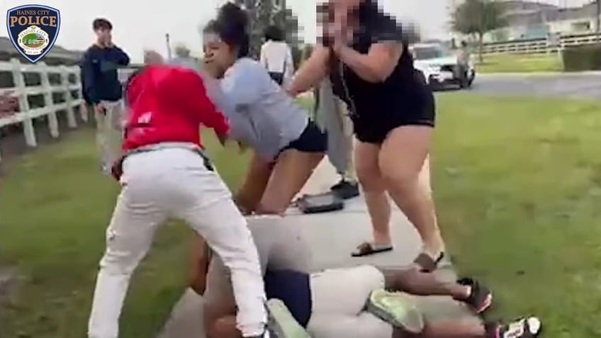 Taitayana Duffy (gray sweatshirt and black shorts) was identified by police as one of the student's guardians and is seen here grabbing one of the students (in a red hoodie).