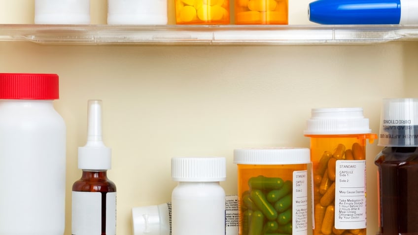 Several containers of over the counter and prescription medications on the shelves of a 1960's medicine cabinet.