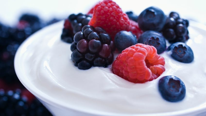 Strawberries and blueberries are on top of a cup of yogurt.