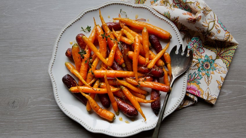 A large platter serving dish of glazed and roasted carrots with fresh thyme and honey