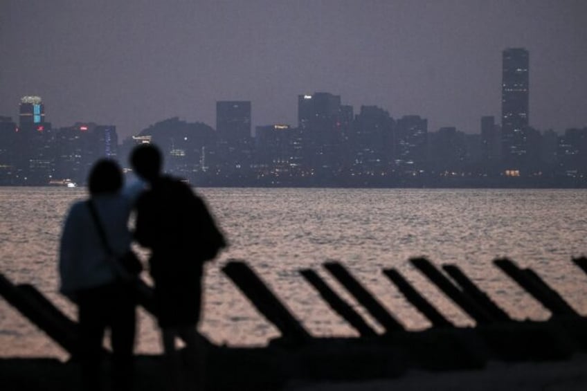 Visitors stand on a beach with anti-landing barricades with the Chinese city of Xiamen see