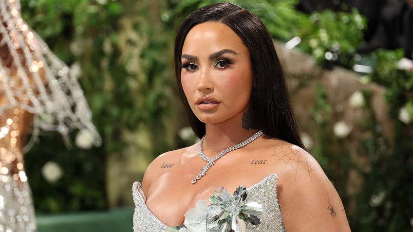 Demi Lovato in a silver sequined dress with flower detail looks directly at the camera on the Met Gala carpet