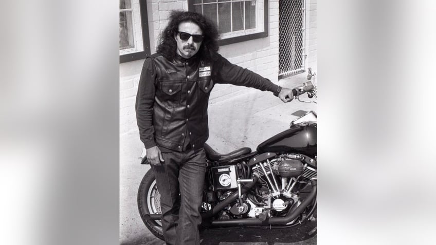 A black and white photo of George Christie standing next to his motorcycle