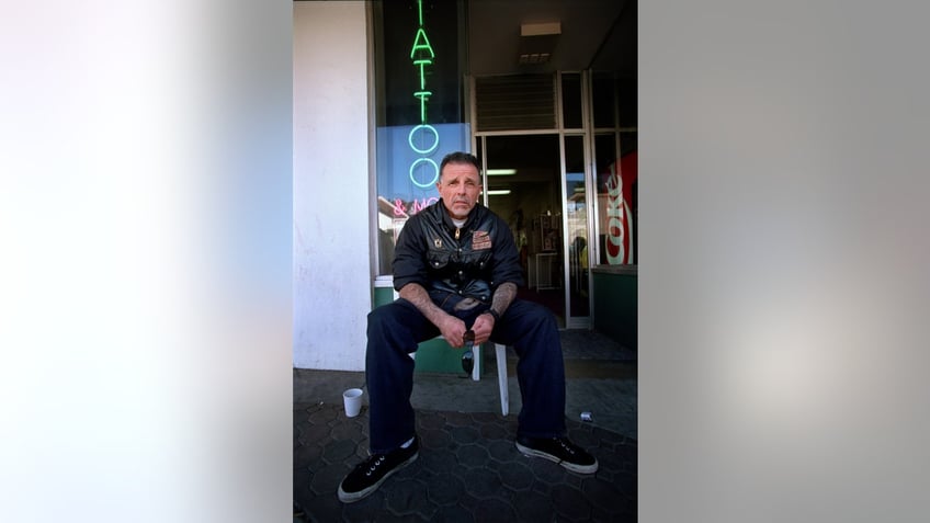 George Christie sitting in front of a tattoo shop.