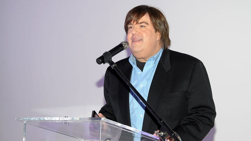 Dan Schneider behind a podium wearing a black suit and blue shirt