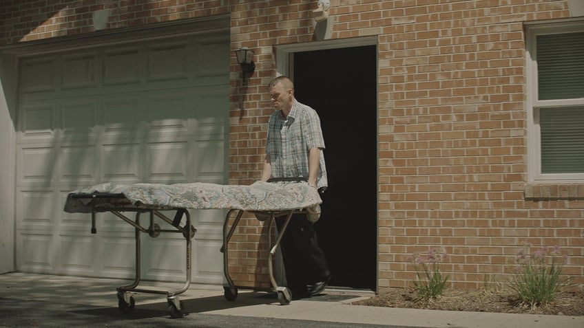 A man pushing a gurney from a home.