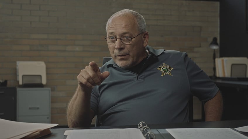 Jeff Jellison wearing a grey shirt and pointing toward the camera.