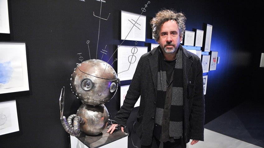 Tim Burton posing next to a piece of his artwork