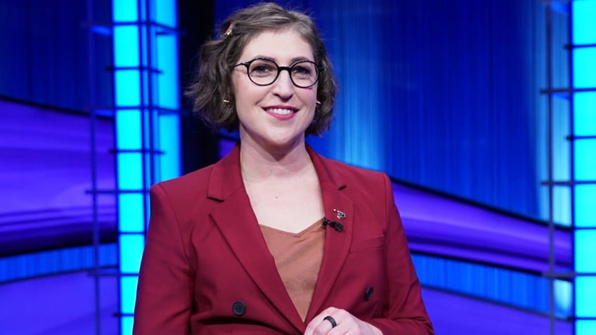 Mayim Bialik in a red pantsuit hosting Jeopardy!