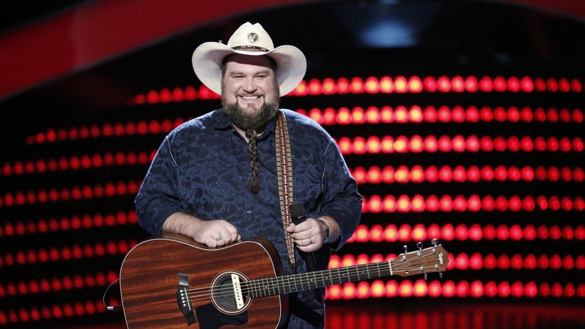 Sundance Head in a blue shirt, tan cowboy hat and dark brown guitar on "The Voice"