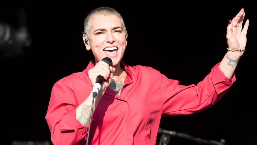 Sinead O'Connor in a red shirt sings on stage in the UK