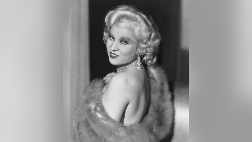 Mae West looks behind her shoulder showing off her shoulder in a black and white photo