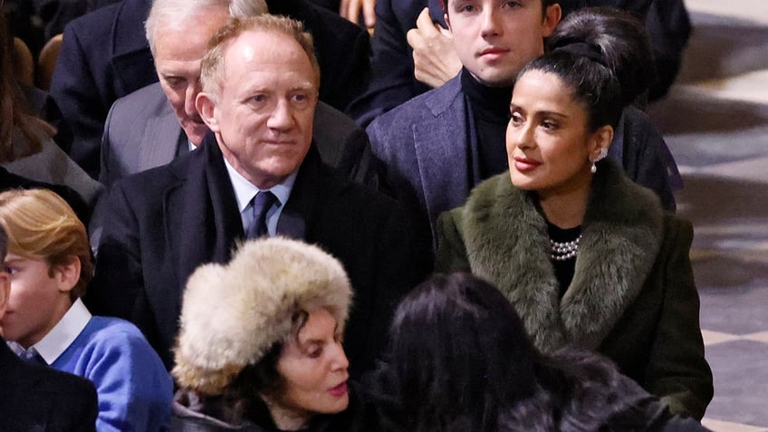 Francois-Henri Pinault in a dark coat sits next to wife Salma Hayek in a green furry jacket at the Notre Dame reopening