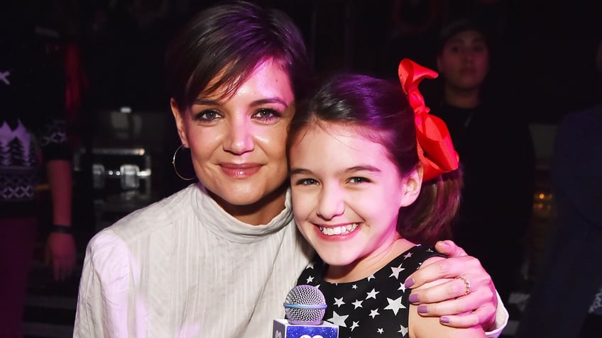 Katie Holmes soft smiles for a photo with young daughter Suri with a red bow in her hair and black dress with stars