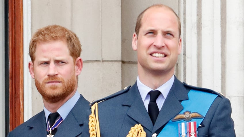 Prince Harry looking sternly at Prince William as they wear matching uniforms at the balcony of Buckingham Palace.