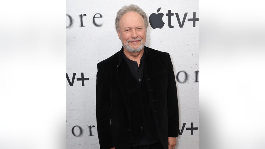 Billy Crystal in a black suit soft smiles on the carpet