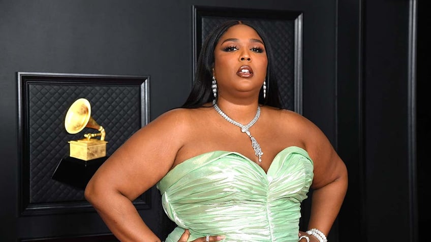 Lizzo in a light green strapless dress stands with her hands on her hips at the Grammys