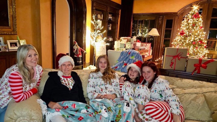 Michael Bolton wearing a Christmas Santa hat snuggles underneath a blanket with family, in Christmas gear