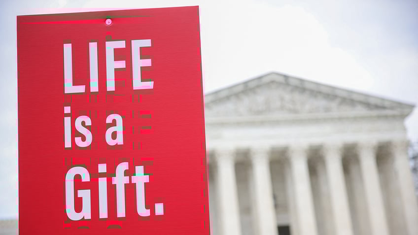 red sign in white letters; LIFE is a Gift; scotus building in background