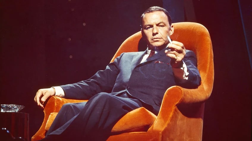 Frank Sinatra sitting on an orange couch holding a cigarette.