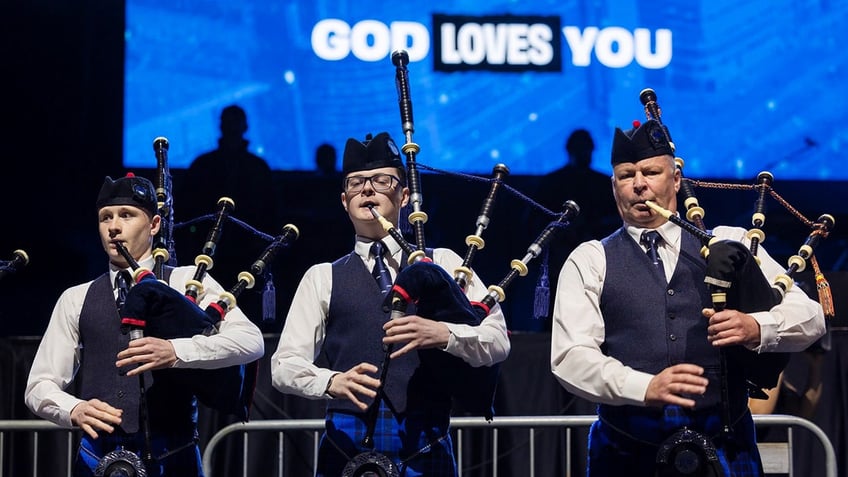 three bagpipers with 'God Loves You' in background on blue