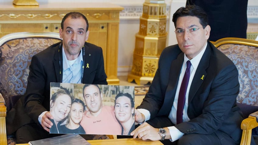 Eli Sharabi and Danny Danon hold a photo showing Sharabi's wife and daughters, who were killed on Oct. 7.