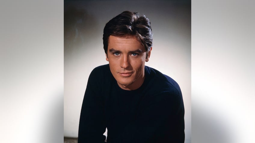 A young Alain Delon in a black shirt looks at the camera