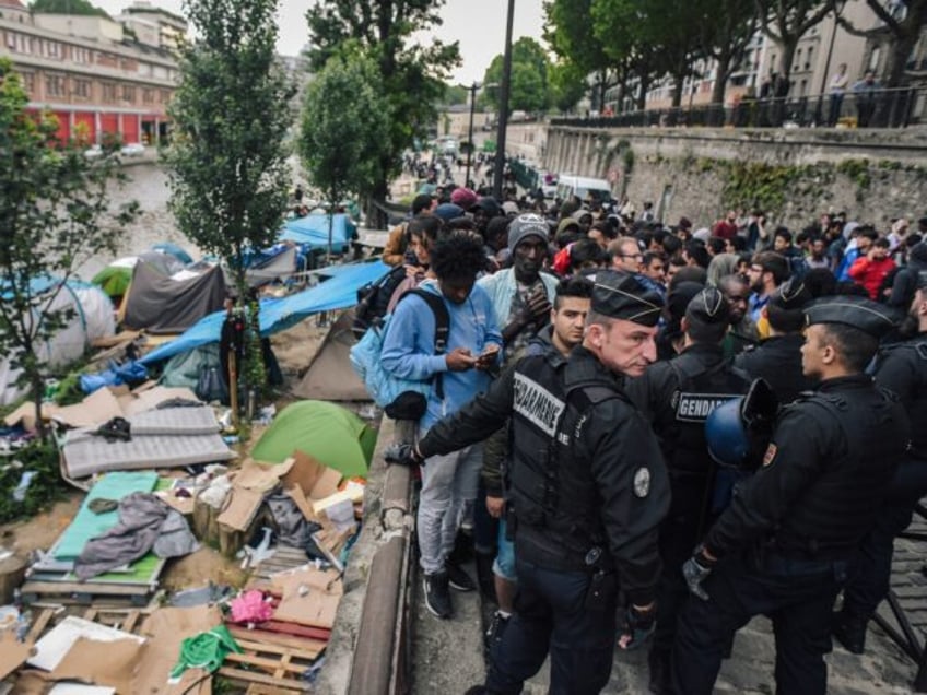 TOPSHOT - French CRS anti-riot police officers stand guard by migrants and refugees queing