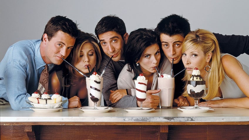 The cast of "Friends" sits behind a bar and sips on milkshakes in a promo shot for the show