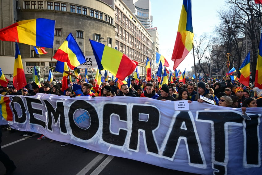 Supporters of nationalist party AUR (Alliance for the Union of Romanians) and of presidential candidate Calin Georgescu hold a banner reading "democracy" as march in Bucharest on January 12, 2024 to protest against the annullement of the second tour of the presidential election asking president Iohannis resign. (Photo by Daniel MIHAILESCU / AFP) (Photo by DANIEL MIHAILESCU/AFP via Getty Images)