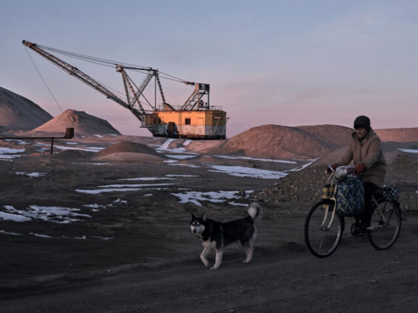 ZHYTOMYR REGION, UKRAINE - FEBRUARY 25: A woman cycles past with her dog as Drag-line exca