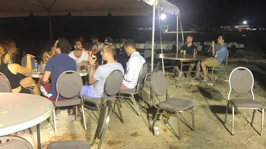 Fyre Festival attendees eat and drink on dirt-covered ground