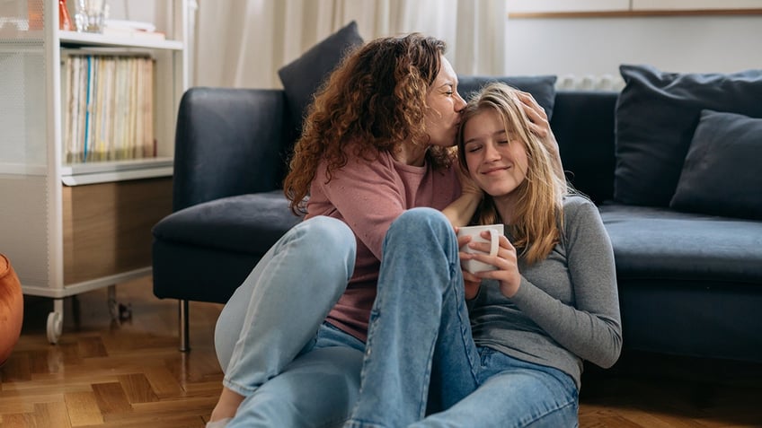 mother kiss her daughter while sitting on floor in living room