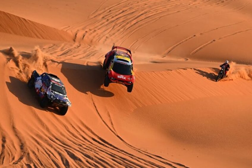 Sebastien Loeb (C) flies past biker Charlie Herbst and Overdrive Racing's Ronan Chabot on his way to victory in a marathon stage 6 of the Dakar Rally