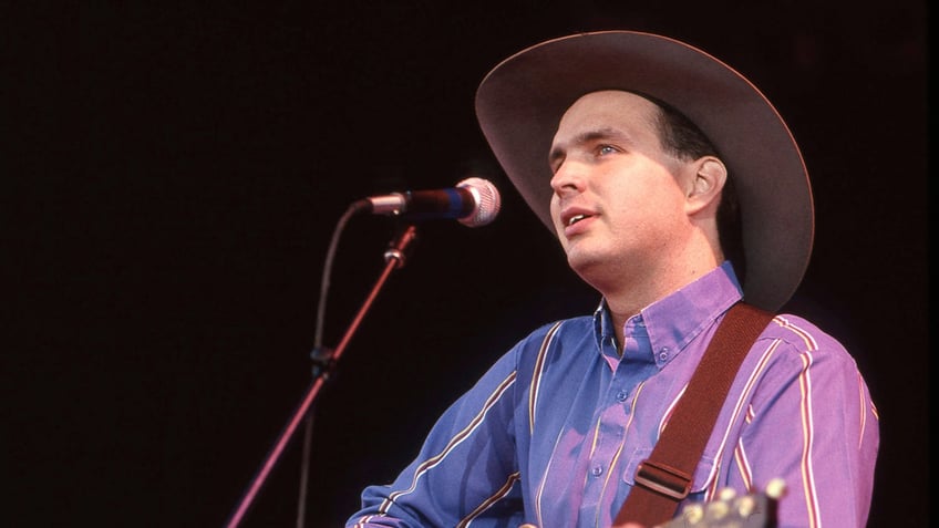 A younger Garth Brooks wears a cowboy hat and sings into a microphone