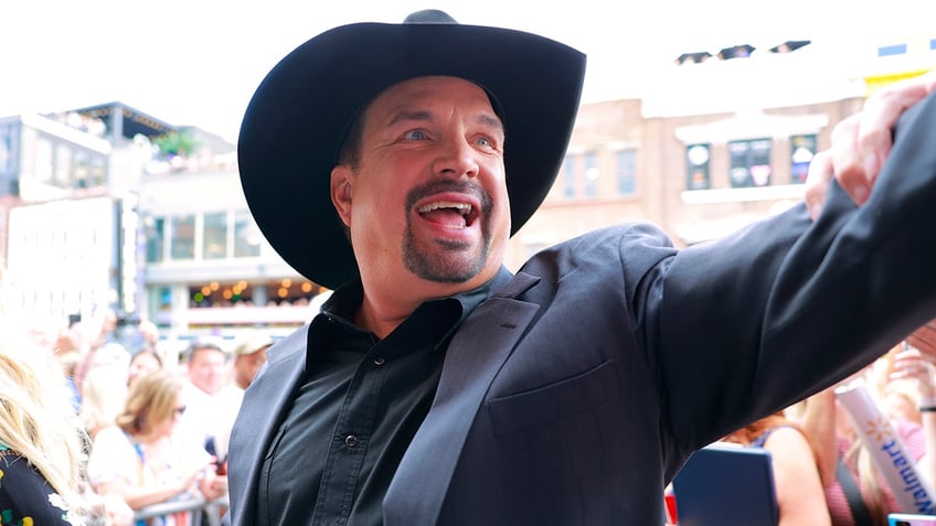 Garth Brooks looks ecstatic as he greets fans wearing a black hat and suit