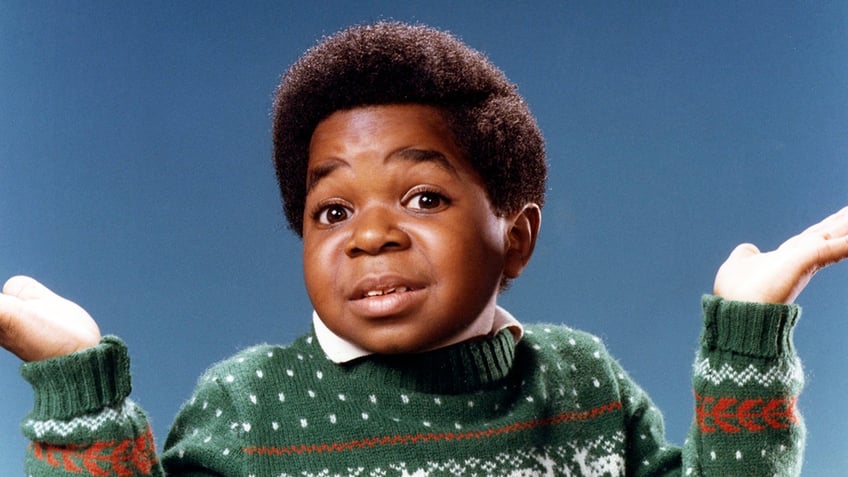 A young Gary Coleman with his green sweater shrugging his hands.