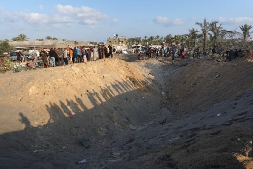 Palestinians stand on the edge of a crater in the Al-Mawasi displacement camp in the Gaza