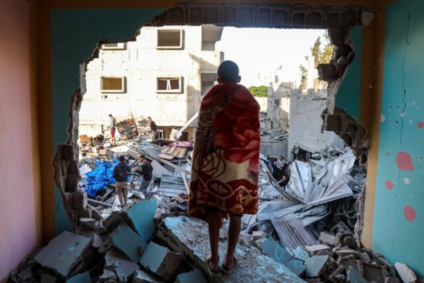 A youth draped in a blanket looks on as people look for survivors in the rubble of a build