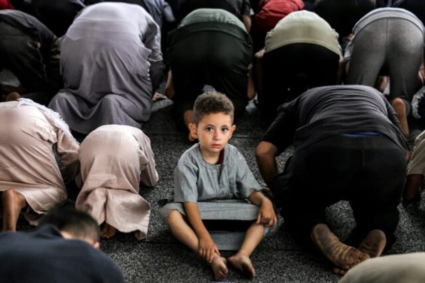 A boy looks on as he sits between Muslim worshippers prostrating as they perform the early